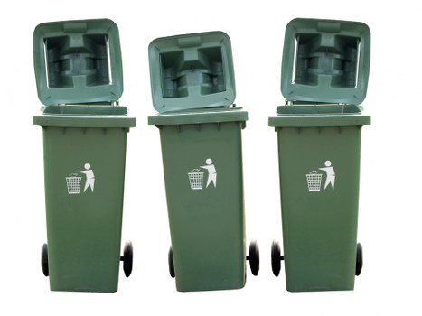 Three green wheeled rubbish bins with open hinged lids are positioned side by side on a paved surface. Each bin features a white pictogram of a person disposing of waste into a bin on its front. The bins are made of plastic and have a textured surface with a smooth, slightly reflective finish, and black wheels visible at the base for mobility. They are situated outdoors, likely on a driveway or pavement, with no other objects visible in the immediate environment. The lighting appears to be natural, suggesting daylight conditions. The arrangement of the bins and their open lids indicate they are ready for waste disposal or collection, aligning with professional rubbish removal services such as those provided by Commercial Waste Lewisham, serving areas around Lewisham and postcode regions in South East London.